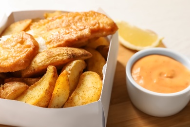 Disposable container with British Traditional Fish and potato chips on wooden board, closeup