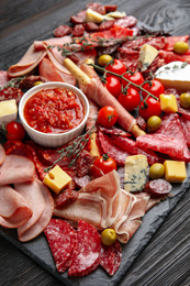 Photo of Tasty ham with other delicacies served on black wooden table