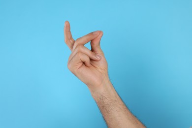 Man snapping fingers on light blue background, closeup of hand