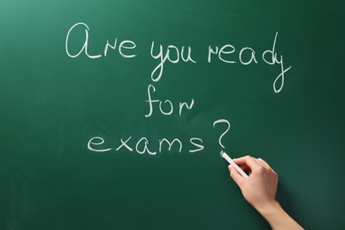 Woman writing phrase Are You Ready For Exams on green chalkboard, closeup