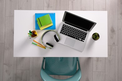 Photo of Chair near white table with laptop, headphones and stationery indoors, top view