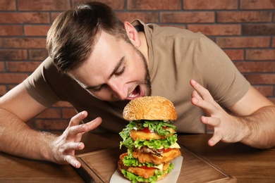 Photo of Young hungry man eating huge burger at table