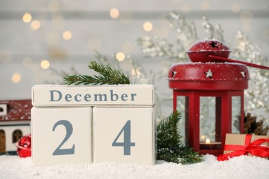 December 24 - Christmas Eve. Wooden block calendar and festive decor on snow against blurred lights