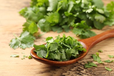 Fresh green cilantro and spoon on wooden table, closeup