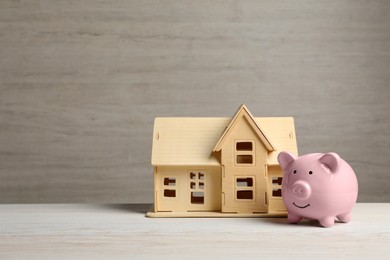 Photo of Piggy bank and little house model on white wooden table. Space for text
