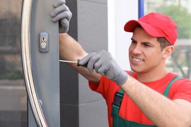 Handyman with screwdriver repairing door lock outdoors