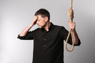 Depressed man with rope noose on light background