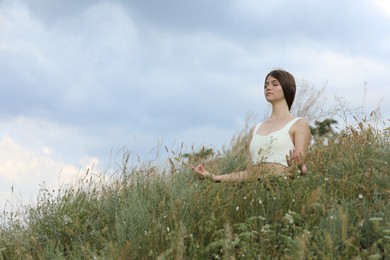 Photo of Teenage girl meditating on hill. Space for text