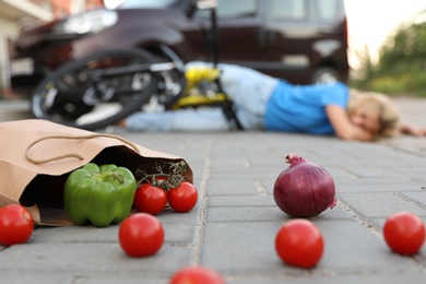 Woman fallen from bicycle after car accident outdoors, focus on scattered vegetables