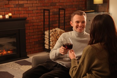 Photo of Happy lovely couple with glasses of wine resting together near fireplace at home
