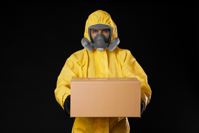 Man wearing chemical protective suit with cardboard box on black background. Prevention of virus spread