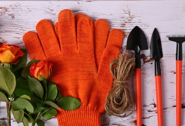 Photo of Gardening gloves, beautiful roses and tools on white wooden table, flat lay