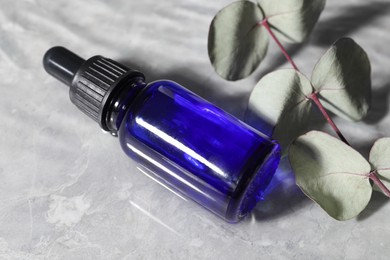 Bottle of face serum and leaves in water on light background, closeup