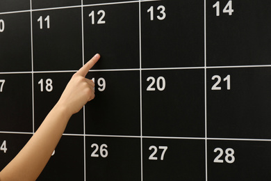 Photo of Woman pointing on date of board calendar, closeup
