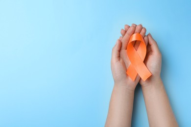 Woman holding orange ribbon on light blue background, top view with space for text. Multiple sclerosis awareness
