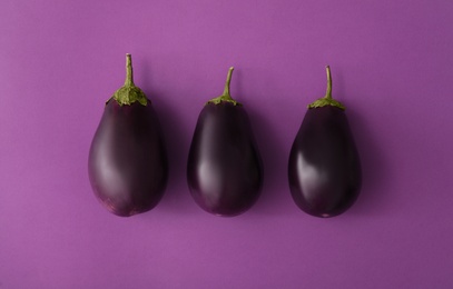 Raw ripe eggplants on purple background, flat lay