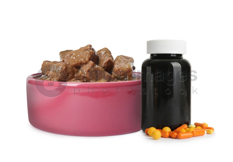Wet pet food in feeding bowl and bottle with vitamin pills on white background