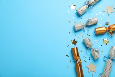Open and closed Christmas crackers with shiny confetti on light blue background, flat lay. Space for text