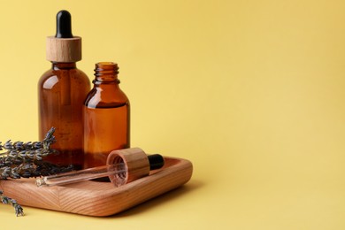 Photo of Wooden tray with bottles of face serum and lavender flowers on yellow background, space for text