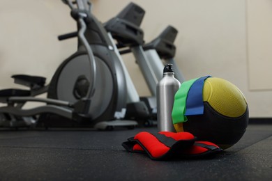 Photo of Medicine ball, bottle, weighting agents and elastic bands on floor in gym, space for text