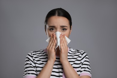 Young woman blowing nose in tissue on grey background. Cold symptoms