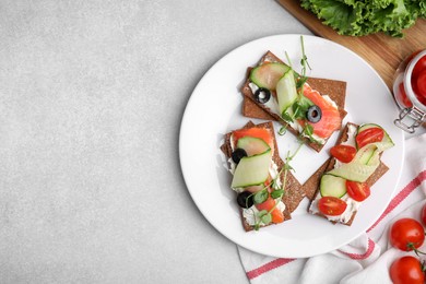Tasty rye crispbreads with salmon, cream cheese and vegetables served on light grey table, flat lay. Space for text