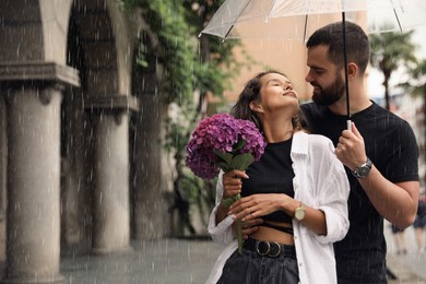 Young couple with umbrella enjoying time together under rain on city street, space for text