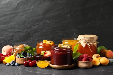 Jars with different jams and fresh fruits on black table