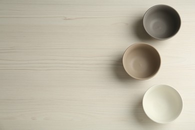 Stylish empty ceramic bowls on white wooden table, flat lay and space for text. Cooking utensils