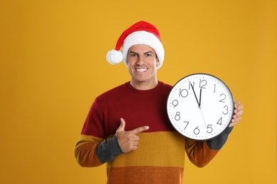 Man in Santa hat with clock on yellow background. New Year countdown