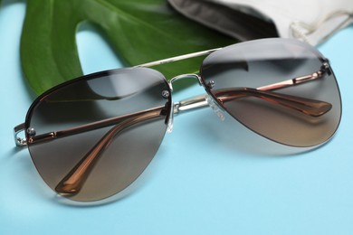 Stylish elegant sunglasses on light blue background, closeup