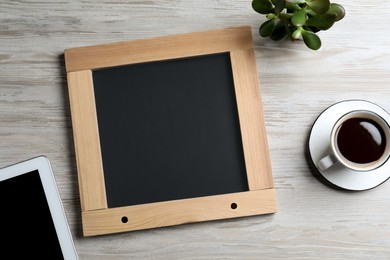 Clean small chalkboard, coffee, plant and tablet on light wooden table, flat lay