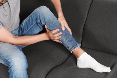 Photo of Man suffering from pain in leg on sofa, closeup
