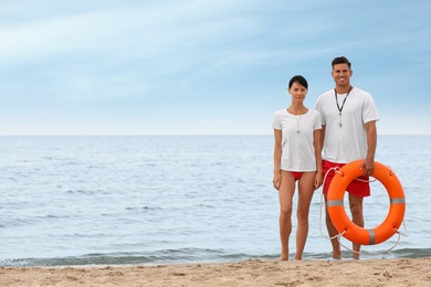 Professional lifeguards with life buoy at sandy beach