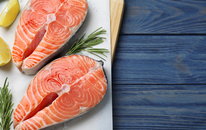 Top view of fresh raw salmon with lemon and rosemary on blue wooden table, space for text. Fish delicacy