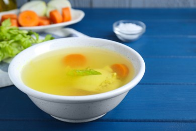 Photo of Delicious chicken bouillon with carrot and celery on blue wooden table, closeup