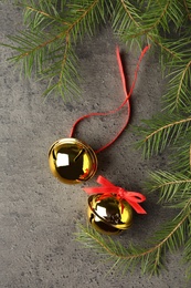 Golden sleigh bells and fir branches on grey background, flat lay