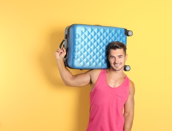 Young man with suitcase on color background