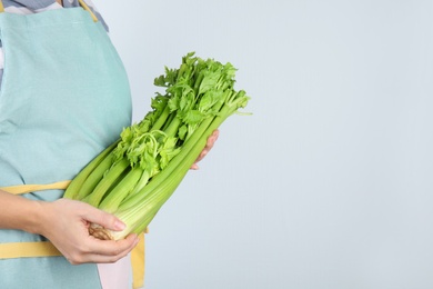Photo of Woman holding fresh green celery on light background, closeup. Space for text