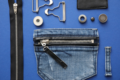 Flat lay composition with garment accessories and cutting details for jeans on blue background