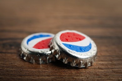 MYKOLAIV, UKRAINE - FEBRUARY 11, 2021: Pepsi lids with water drops on wooden background, closeup