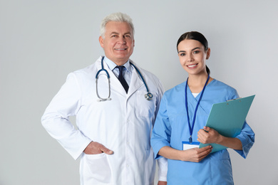 Senior doctor and young nurse against light background