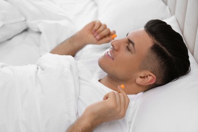 Man inserting foam ear plugs in bed