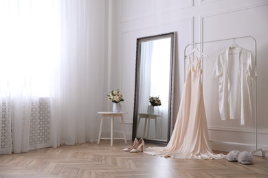 Elegant wedding dress and silk robe hanging on rack in room