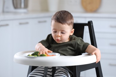 Cute little baby eating healthy food in high chair at home