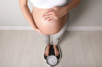 Pregnant woman standing on scales indoors, above view