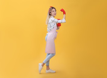 Young housewife in gloves on yellow background