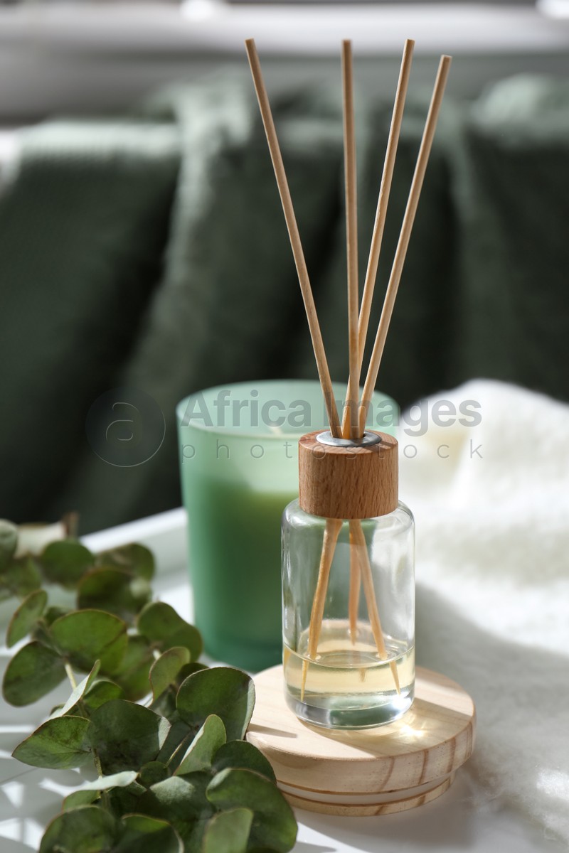 Reed air freshener, candle and eucalyptus branches on tray indoors