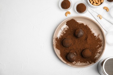 Delicious chocolate truffles with cocoa powder and nuts on white table, flat lay. Space for text