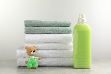 Photo of Bottle of laundry detergent, stacked fresh towels and knitted bear toy on grey table